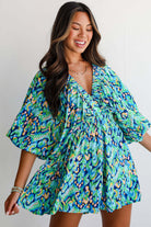 Woman in green and blue abstract print puff sleeve romper, showcasing playful summer style.