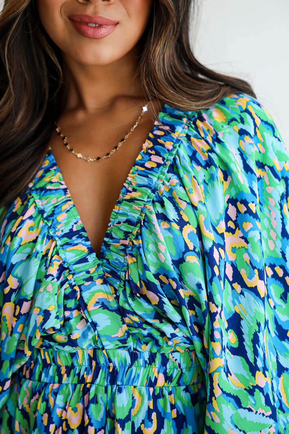 Close-up of a woman in a green and blue abstract print romper with a V-neck and puff sleeves.