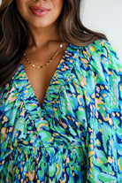 Close-up of a woman in a green and blue abstract print romper with a V-neck and puff sleeves.