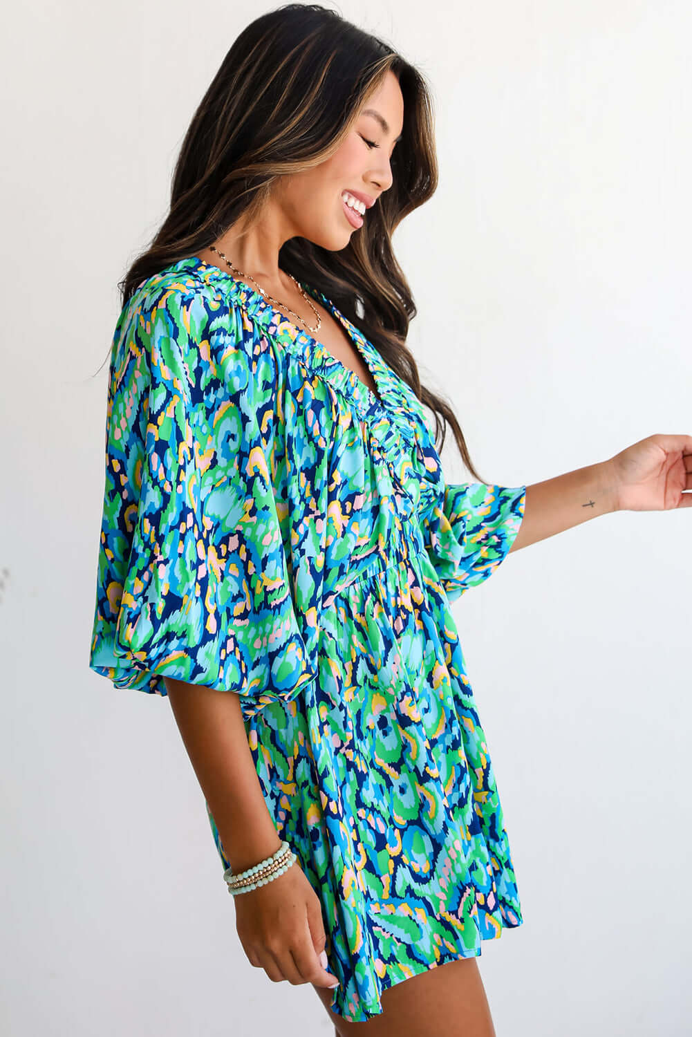 Model wearing the Wave Dancer Romper in a vibrant green and blue abstract print, showcasing a flattering V-neckline and puff sleeves.