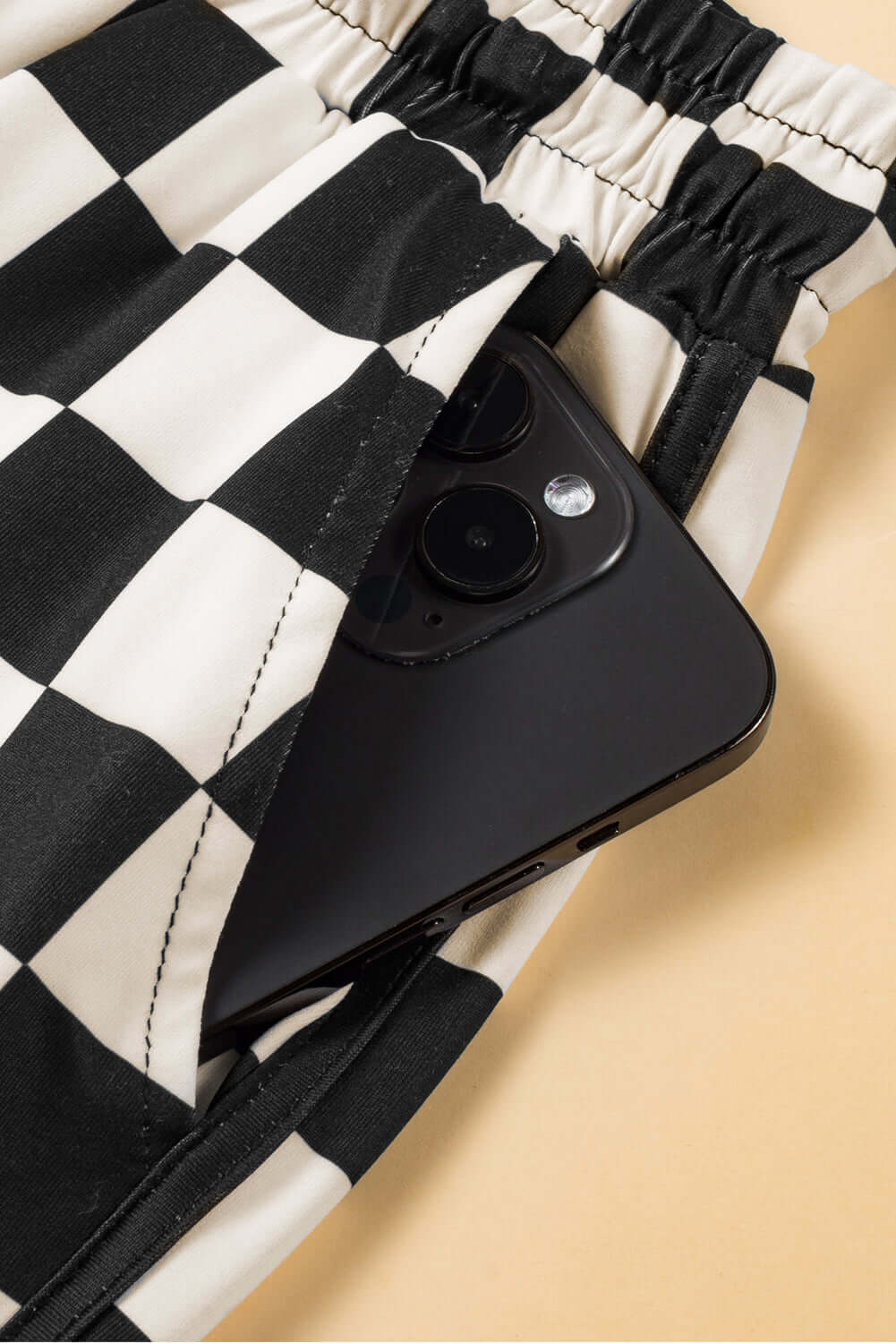Close-up of black checkered shorts with a smartphone tucked into the pocket for a stylish, casual look.