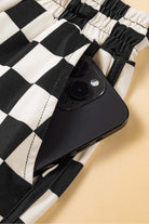 Close-up of black checkered shorts with a smartphone tucked into the pocket for a stylish, casual look.
