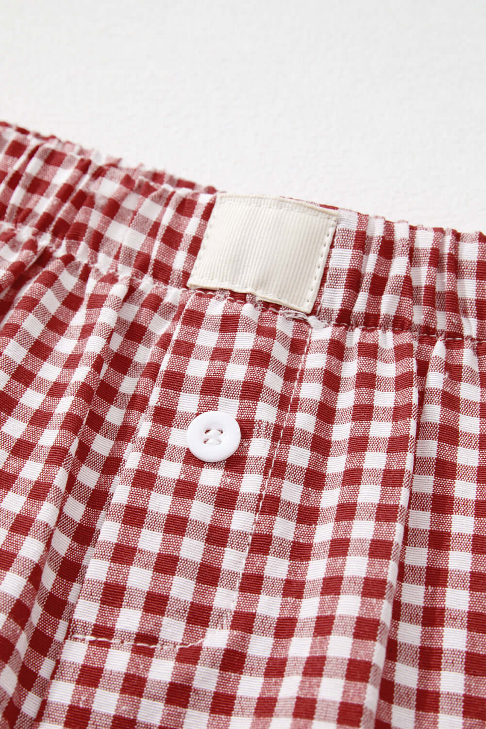 Close-up of red gingham high waist shorts featuring an elastic waistband and button detail.