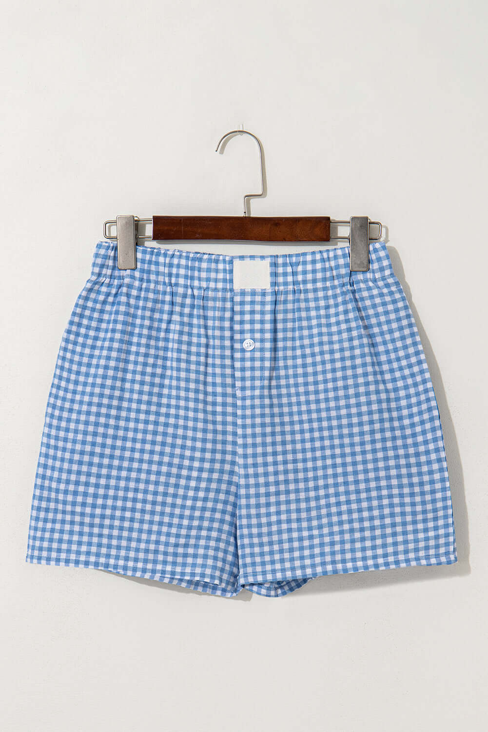 Blue gingham high waist shorts hanging on a wooden hanger, perfect for summer picnics and casual wear.