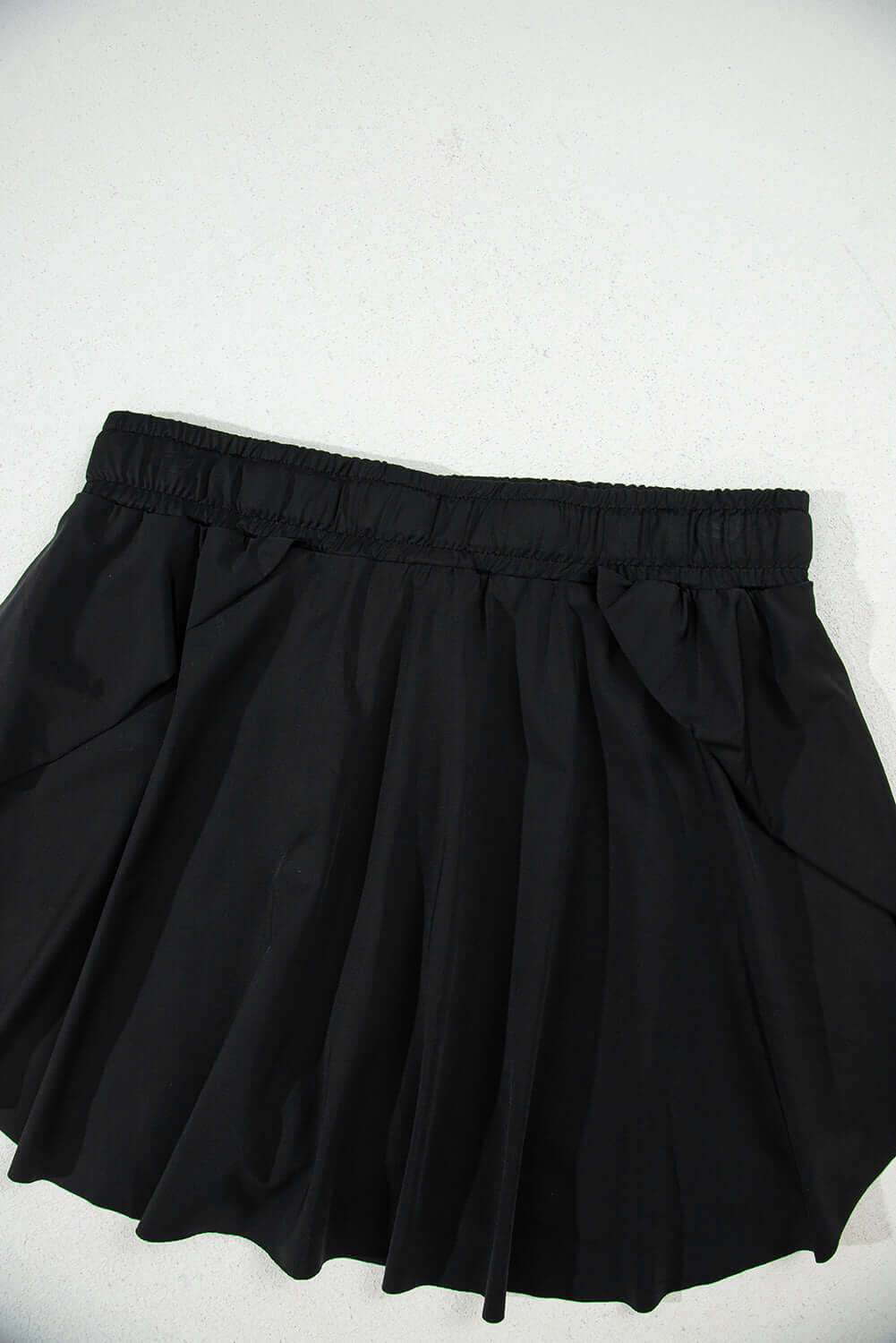 High-waisted black skort with stretchy waistband and flowy overlay for sporty and stylish looks.