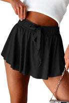 Black high-waisted skort with a flowing overlay and stretchy waistband for sporty style and comfort.