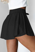 High-waisted black skort with a flowy overlay and stretchy drawstring waistband, ideal for sporty activities.