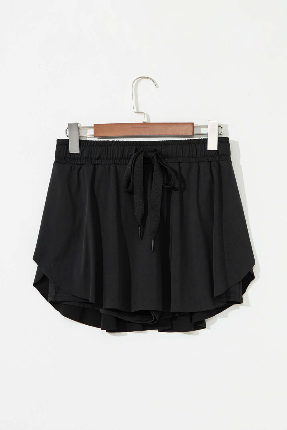 Black high-waisted skort with stretchy drawstring waistband and flowy overlay, perfect for sporty style.