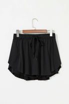 Black high-waisted skort with stretchy drawstring waistband and flowy overlay, perfect for sporty style.