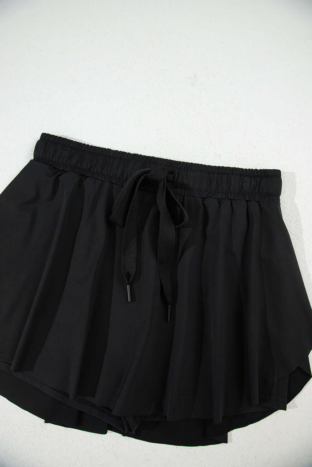 Black high-waisted skort with a stretchy waistband and flowy overlay, perfect for sporty and casual wear.