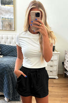 Stylish woman wearing a white t-shirt and black French terry drawstring skort in a chic home setting.