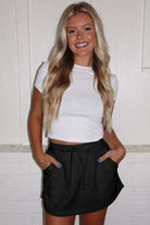 Model wearing Skort Story black skort, styled with a white crop top, showcasing a casual look.