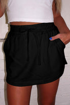 Model wearing a black French terry drawstring skort with pockets paired with a white crop top.