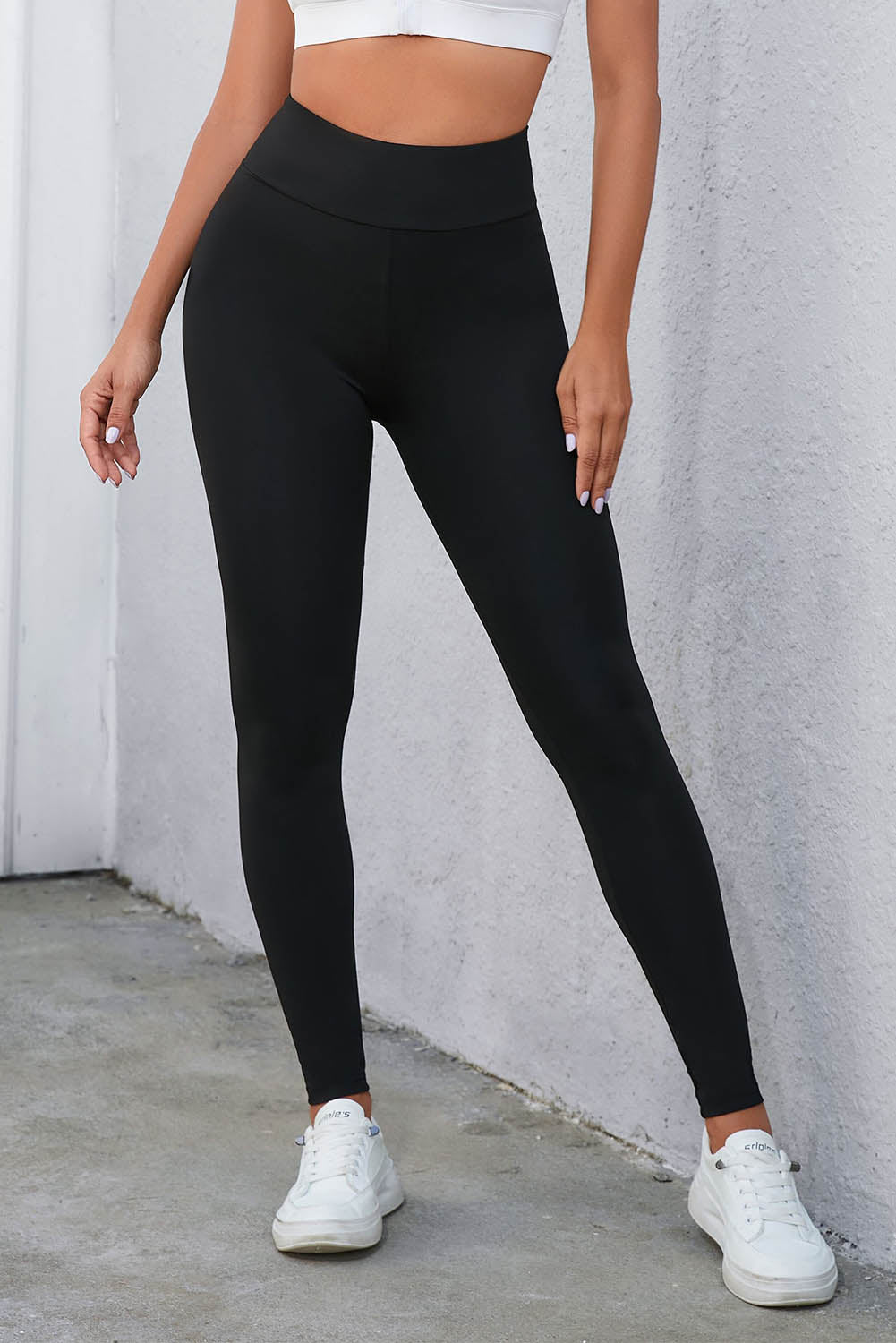 High-waisted black leggings with tummy control and crisscross detail, paired with a white top and sneakers for a versatile style.