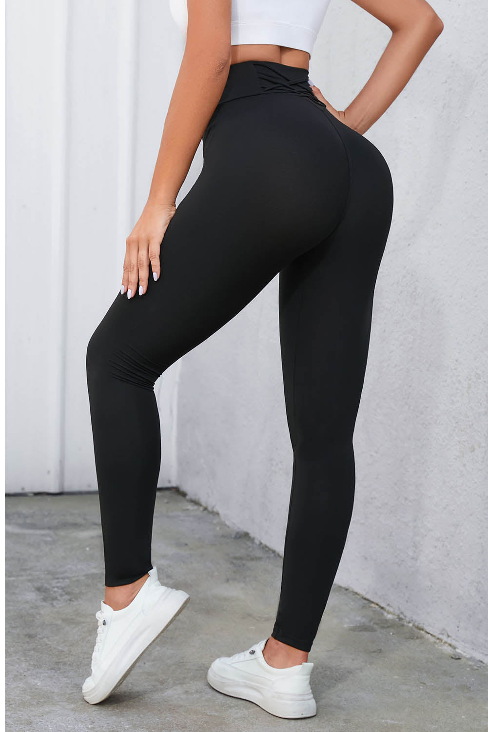 High-waisted black leggings with crisscross detail, offering a flattering fit and tummy control, styled with white sneakers.