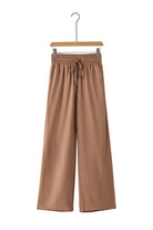 Caramel Latte wide leg pants with smocked waist and side pockets hanging on a wooden hanger.