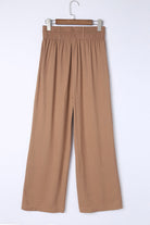 Caramel Latte wide leg pants with smocked waist and side pockets, 65% viscose and 35% polyester, hanging on a wooden hanger.