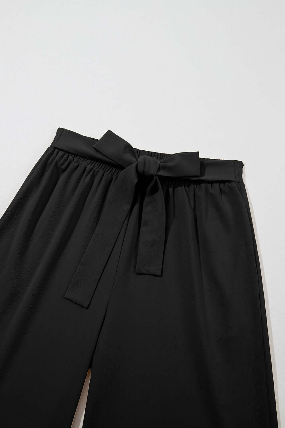 Close-up of black wide leg pants with tie-front sash and elastic waistband, ideal for stylish comfort.