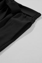 Close-up of black wide-leg pants showing a tie-front sash and textured fabric detail.