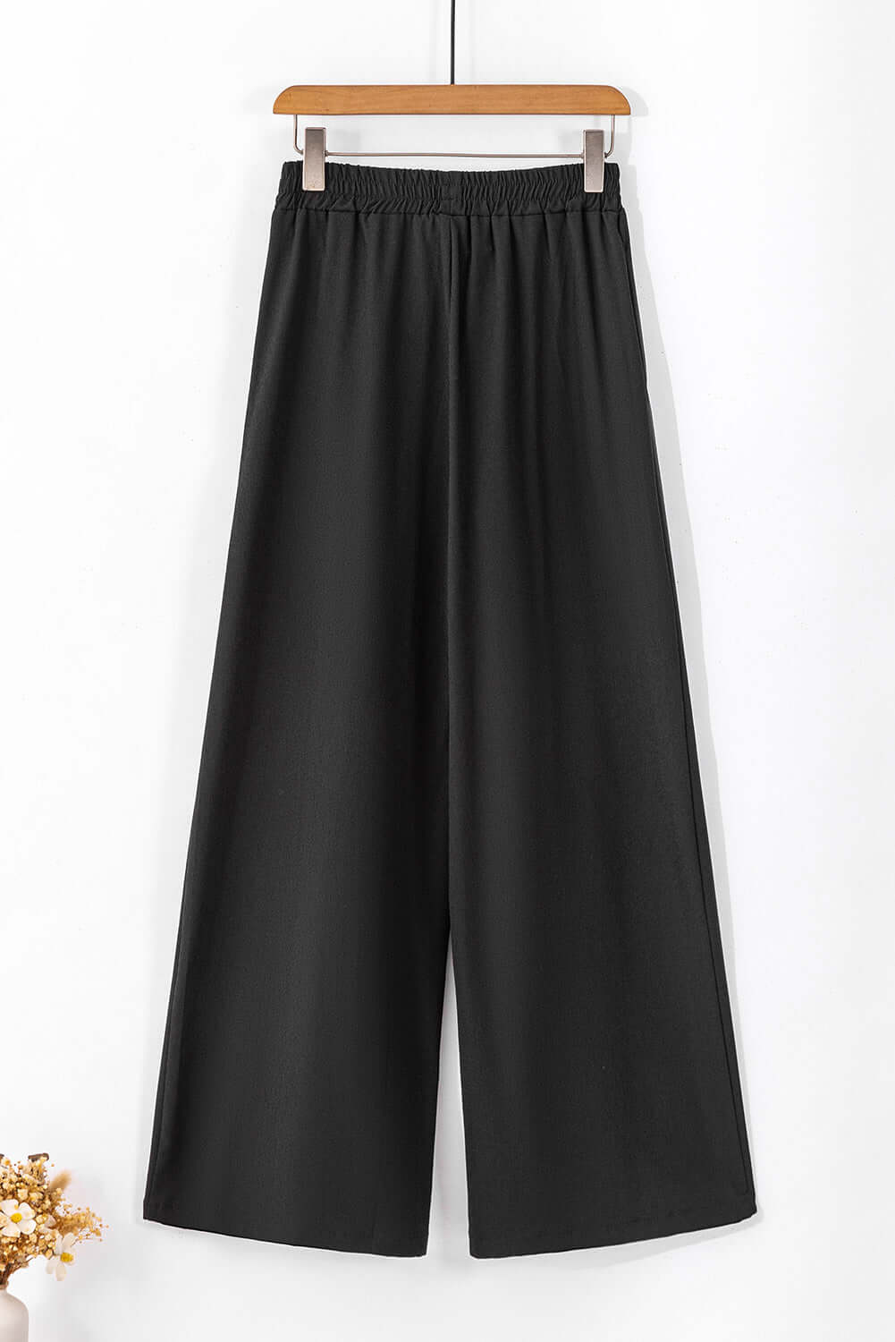 Black wide-leg pants hanging on a wooden hanger, featuring an elastic waistband and flowy design.