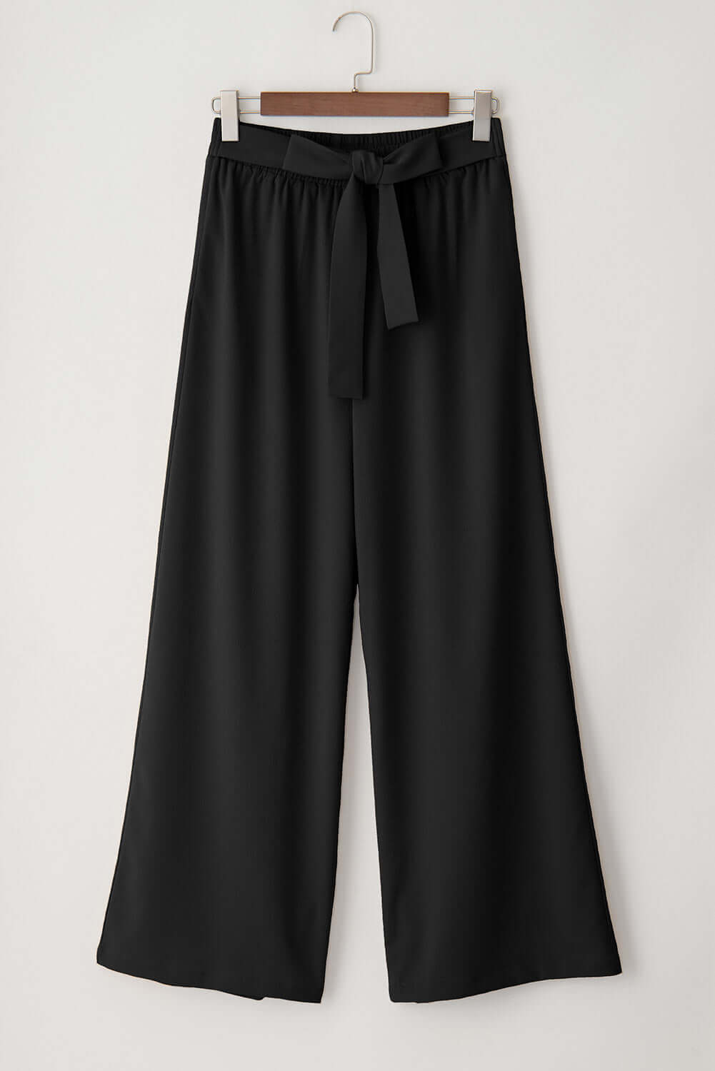 City Sway wide leg pants in black with a tie front sash hanging on a wooden hanger.