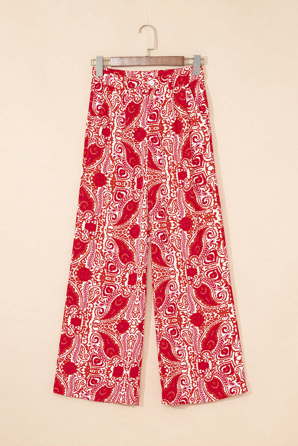 Red and cream wide leg pants with abstract paisley motif hanging on a beige background.