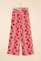 Red and cream wide leg pants with abstract paisley motif hanging on a beige background.