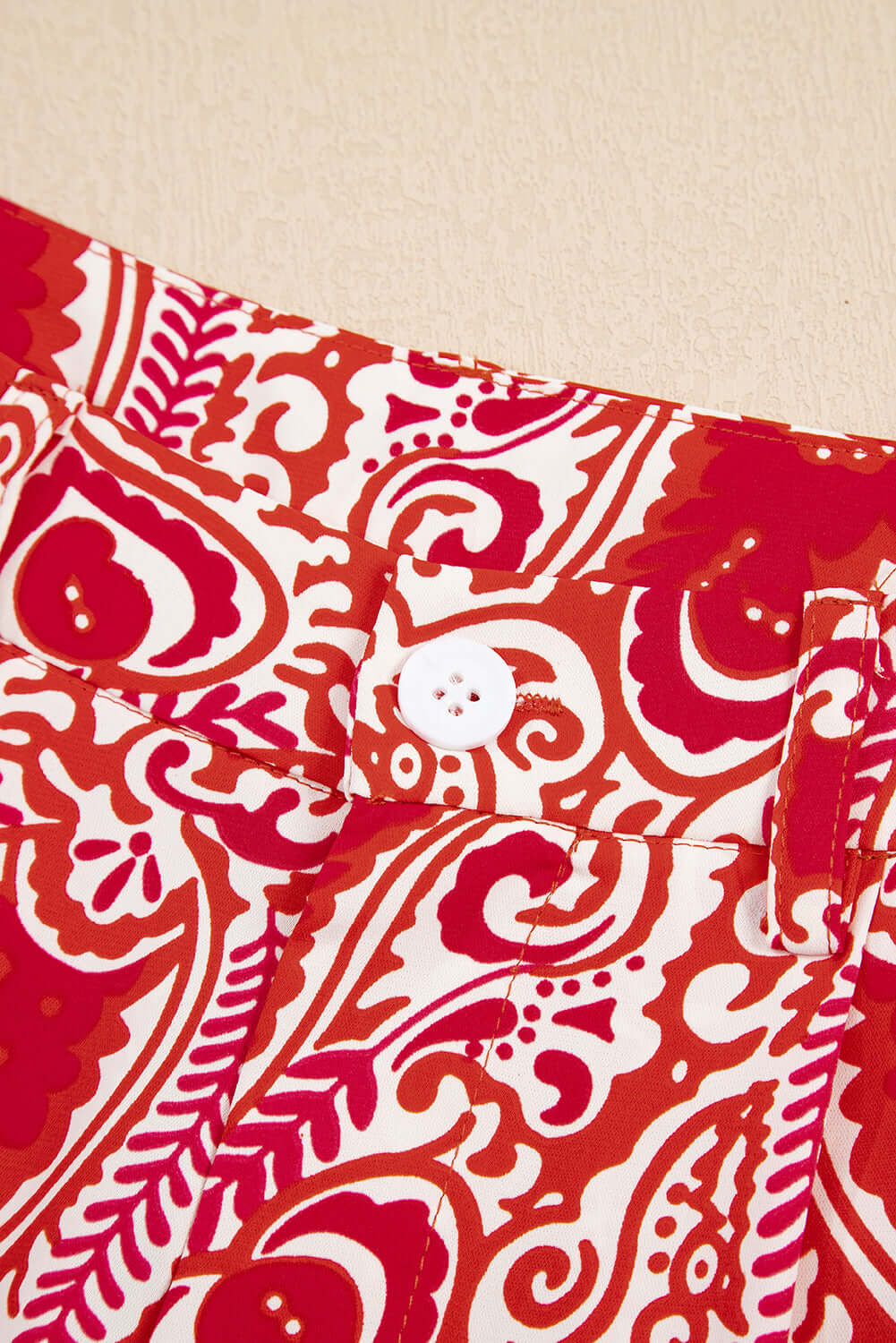 Close-up of Boho Glam Wide Leg Pants button and abstract red & cream fabric design.