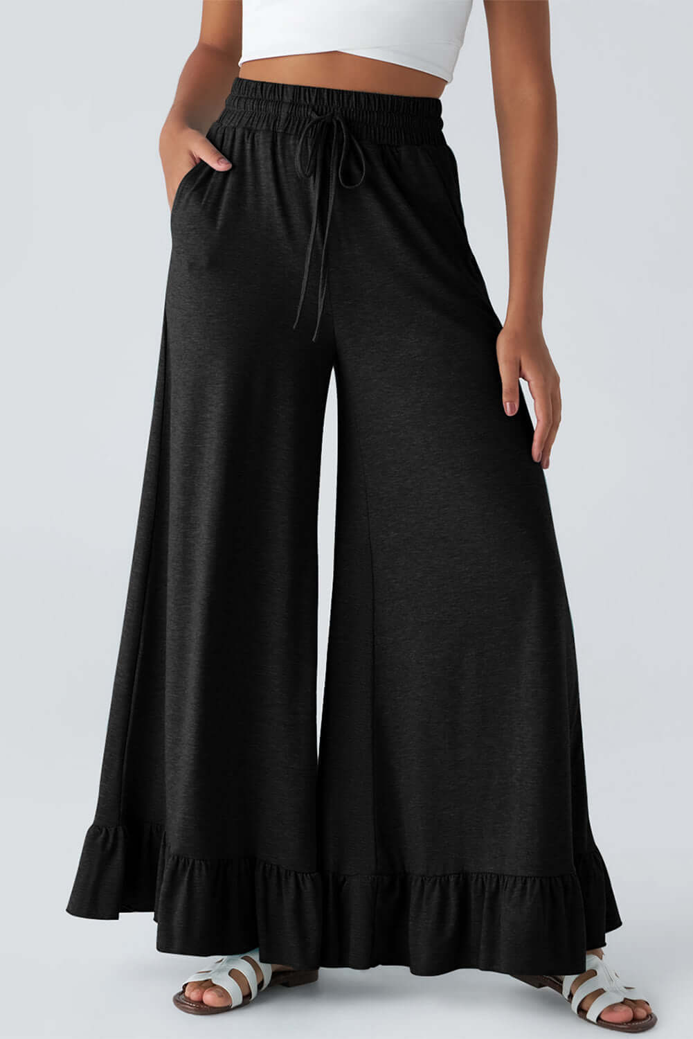 CHANTED COMFORT WIDE LEG PANTS model wearing black wide leg pants with ruffled hem and pockets.