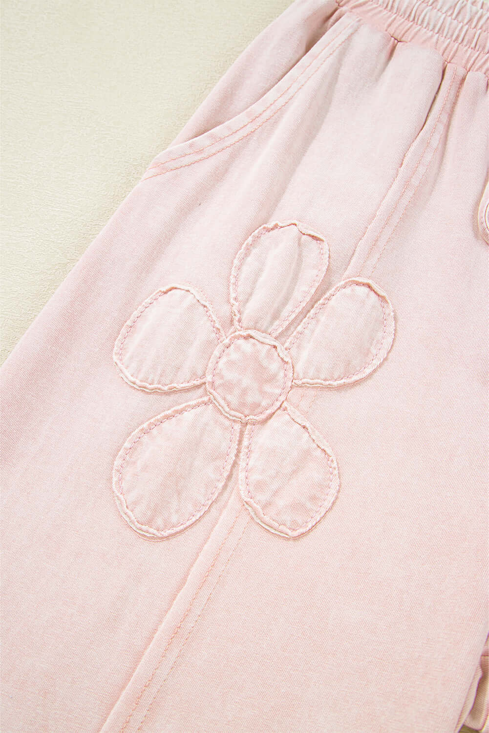 Close-up of pink cropped wide leg pants with embroidered flower patch detail.