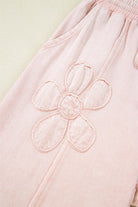 Close-up of pink cropped wide leg pants with embroidered flower patch detail.