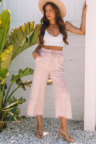 Model wearing pink Daisy Daydreamer pants with flower patches, styled with a white crop top and a wide-brimmed hat.