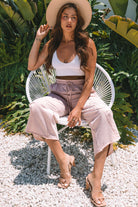 Model wearing Daisy Daydreamer cropped pants and white top, seated outdoors in a tropical setting.