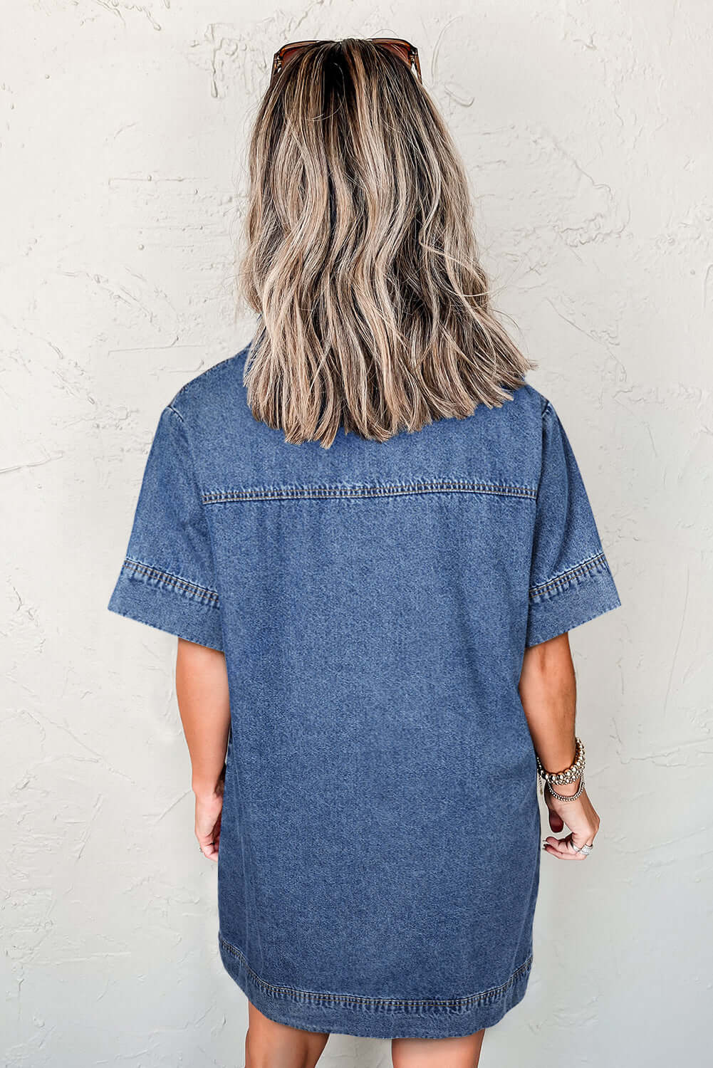 Back view of a woman in a short-sleeve blue jean dress, showcasing relaxed fit and denim texture.