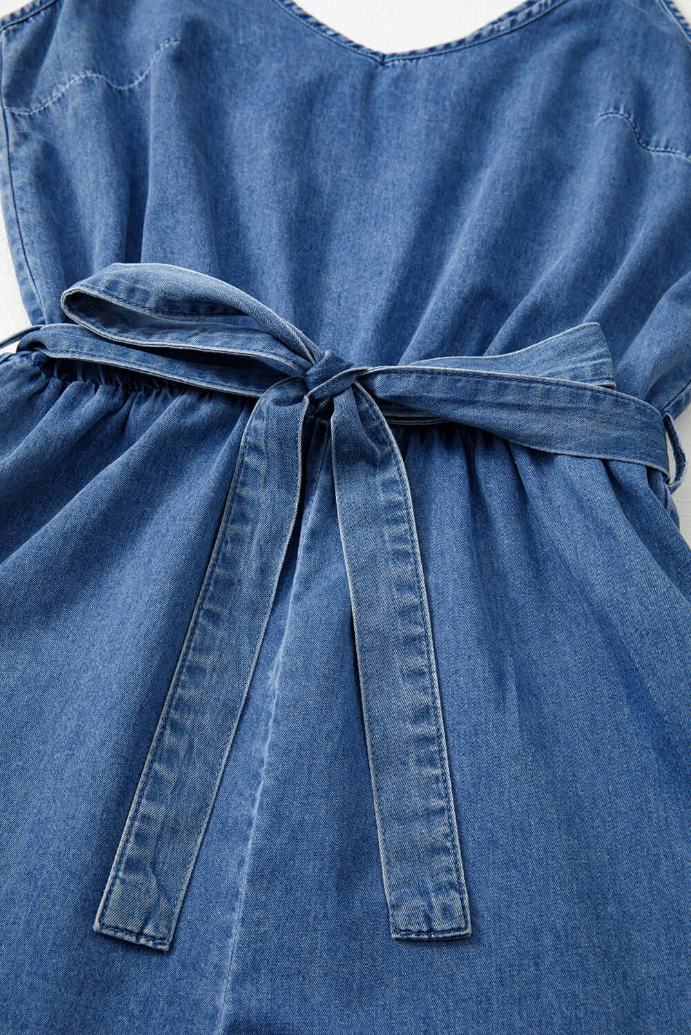Close-up of the back of Shore Thing Denim Romper featuring a tied waist and medium blue chambray fabric.