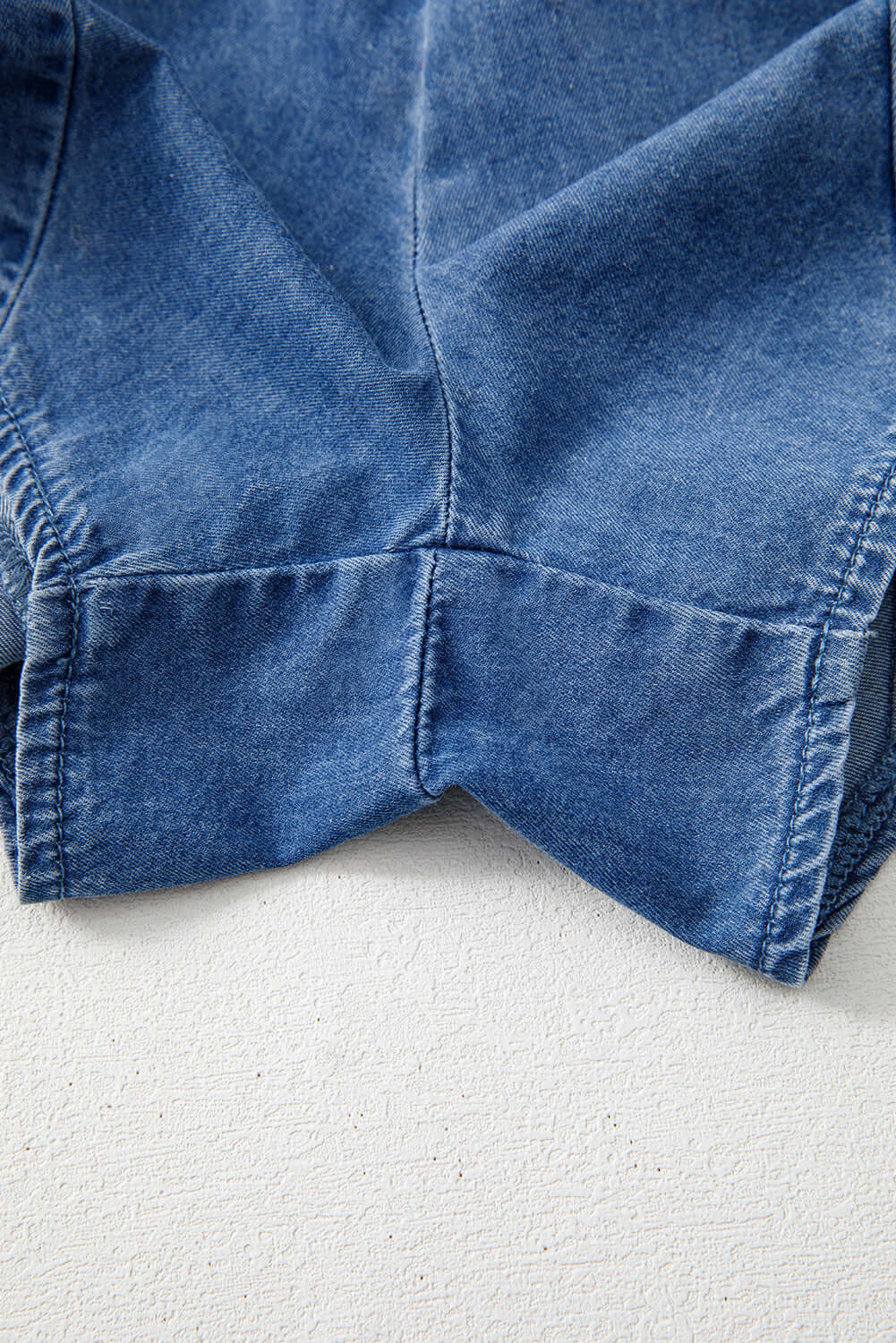 Close-up of the Shore Thing Denim Romper showcasing its medium blue wash and stylish stitching details.