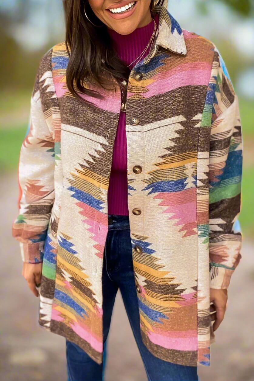 Woman wearing PAINTED DESERT Jacket with vibrant Aztec print and button-up design, styled with a pink top and jeans for a chic look.