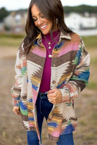 Woman wearing a PAINTED DESERT Jacket with vibrant Aztec print, paired with a magenta top and jeans, smiling outdoors.