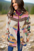 Woman wearing PAINTED DESERT Jacket with vibrant Aztec print, buttoned up over a purple top, stylishly paired with jeans outdoors.