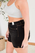 Model showcasing Judy Blue Sassafras shorts with black fabric, brown stitching, and versatile styling options.