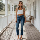 Model wearing RISEN FALLON MID RISE JEANS (dark) with a fitted white crop top on a porch.
