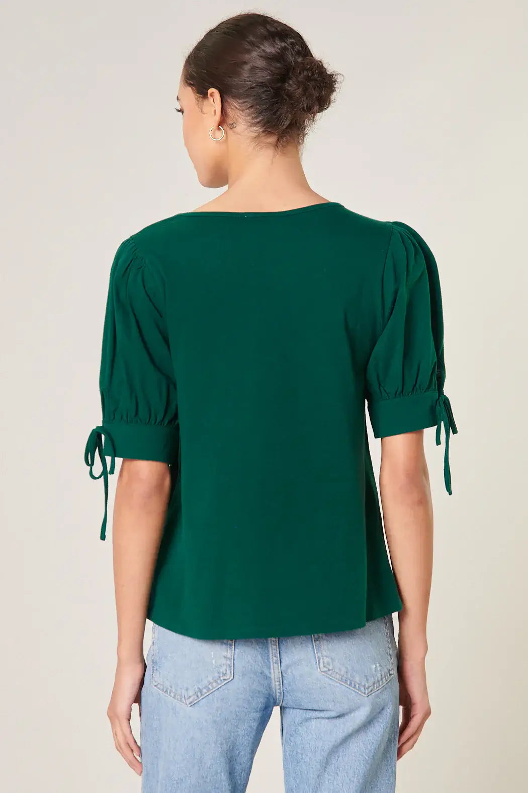 Back view of emerald green EMERALD ENCOUNTERS TOP with puff sleeves and tie details, styled with jeans.