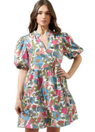 Model wearing the Jacey Dress by Sugarlips featuring a vibrant floral pattern and ruffled neckline.