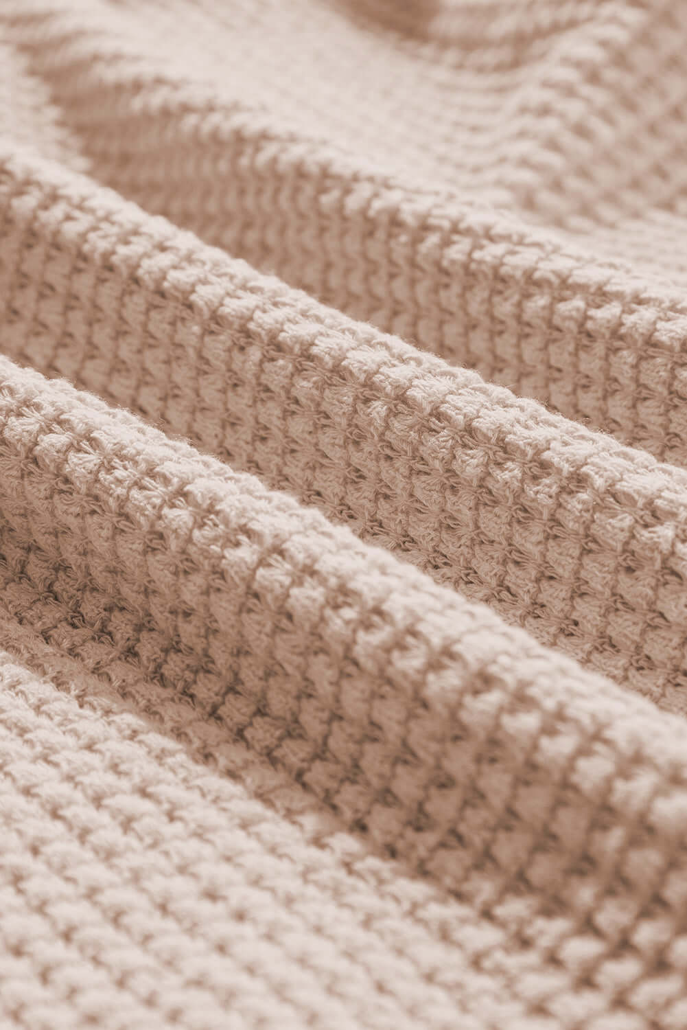 Close-up of textured beige fabric showcasing a knit pattern, ideal for fashion and textile applications.