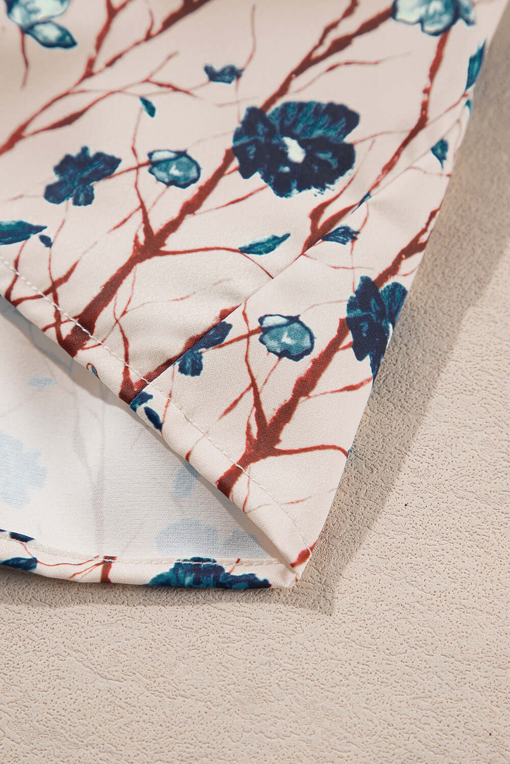 Close-up of delicate floral print fabric featuring shades of blue and red on a soft background. Perfect for stylish tops.