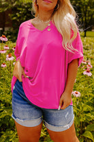 Plus size woman wearing a hot pink V-neck top with cuffed sleeves, paired with denim shorts in a flower garden.