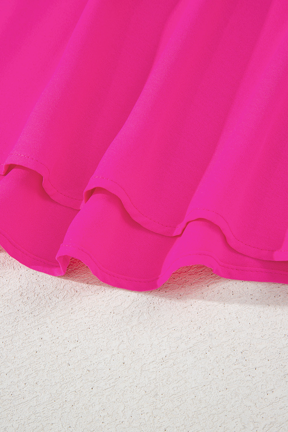 Close-up of the Berry Brilliance hot pink top's high-low hemline, showcasing its vibrant color and flowing fabric.