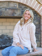 Woman wearing ivory Simply Luxe Pullover with quarter zip and PU leather logo, sitting by a stone fireplace, showcasing cozy winter style.