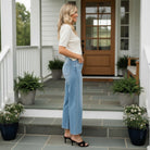 Woman wearing RISEN- BREE JEANS, high rise wide crop jeans, standing on a porch in casual stylish attire.
