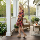Woman wearing UNSTOPPABLE YOU DRESS - Jodifl, standing on a porch with a floral design and smiling confidently.